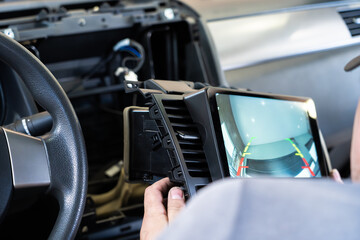 Car electrician installing modern multimedia system with rear view camera. Dashboard wiring, parking safety, touchscreen display, vehicle electronics upgrade and smart technology integration.