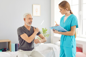 Obraz premium Mature senior man sitting on couch in modern rehab clinic and complaining of pain in the shoulder to a young nurse or doctor physiotherapist. Physiotherapy and physical rehabilitation concept.