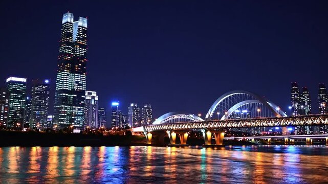 lengthy illuminated suspension bridge traversing waterway set against panoramic metropolitan vista after dark, hosting international athletic competitions