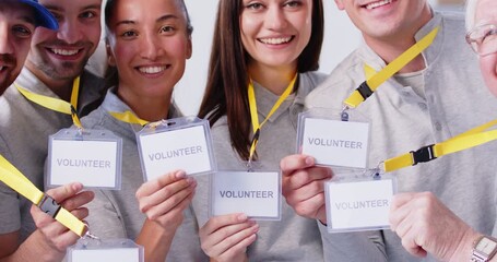 Team happy diverse multiethnic multiracial volunteers in grey uniform T shirts holding paper name tag ID cards on yellow lanyards looking at camera smiling saying something about charity work together