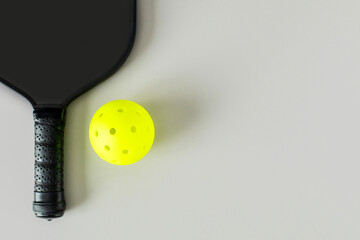 Close-up of a black pickleball paddle and bright yellow ball on light neutral background, photographed from above with copy space..