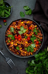 Tex-mex meet chili con carne with beef, red beans,, sweet corn, cilantro in frying pan, rusty green background top view