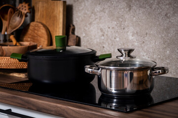 Steel pots on induction hob on cozy modern kitchen with cooking utensils, pots, cutting boards on...