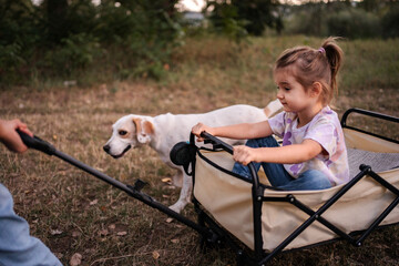 Obraz premium Parent pulling toddler in cart with dog walking alongside