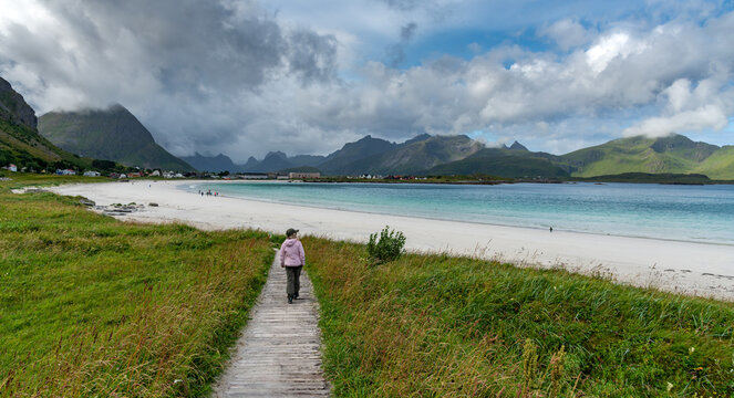 Tourist walking on ramberg beach, lofoten islands, norway, on cloudy summer day