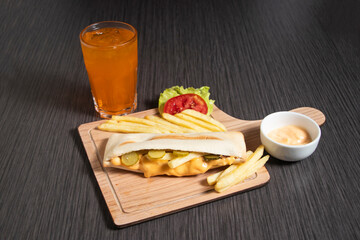 Delicious chicken sandwich meal with melted cheese, pickles and fries on wooden board with Mayonnaise dipping sauce and orange drink side view of fast food