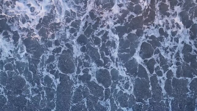 Aerial Top Down View of Deep Blue Ocean Waves and White Foam Textures. Stunning Drone Footage Capturing the Powerful Movement of Sea Water and Natural Bubble Patterns from a High Angle Perspective.