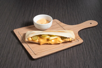 Delicious chicken sandwich with melted cheese, pickles and fries on wooden board with Mayonnaise dipping sauce side view of fast food