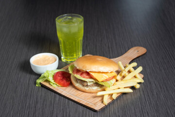 Delicious crispy chicken burger meal with melted cheese, fresh lettuce, tomato, soda drink, fries, and mayo sauce on wooden board side view of fast food