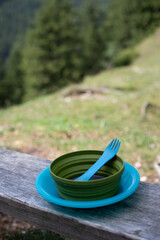 Collapsible camping bowl and spork on wooden bench in mountain landscape