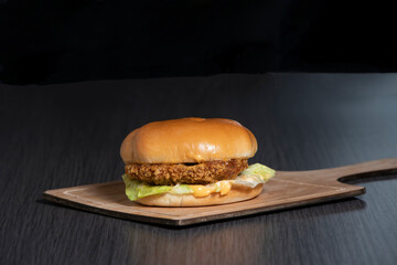 crispy taza burger with melted cheese, lettuce leave, soft bun and special sauce on wooden board side view of fast food