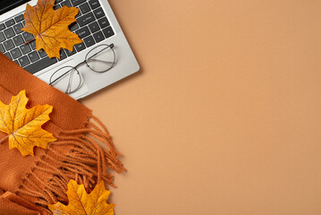 Flat lay of a laptop, autumn leaves, eyeglasses, and a warm scarf on an orange background