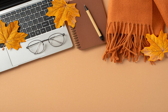 Flat lay of an autumn-inspired workspace featuring a laptop, notebook, reading glasses, and decorative fallen leaves on a warm orange surface.