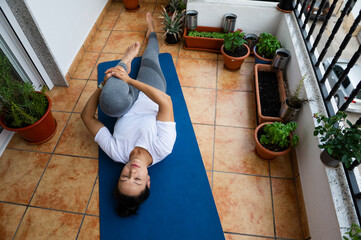 Woman Practicing Yoga At Home on a Balcony With Potted Plants Around