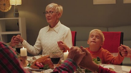 Family holding hands and praying before thanksgiving dinner