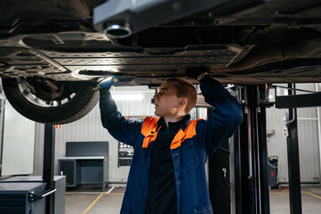 Young mechanic inspecting car chassis using flashlight and holding tablet in a modern workshop