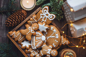 Handmade zero waste gift for Christmas or New Year. Wooden box with homemade delicious gingerbread cookies decorated with white icing. Cozy home atmosphere, fairy lights, fir tree branches