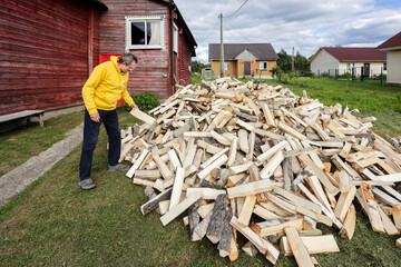 Mature man inspects pile of firewood dumped from truck in front of rural house.