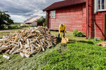Adult man takes firewood from pile and places it into basket.