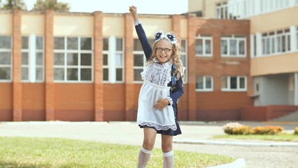 Excited schoolgirl raising her hand, celebrating the beginning of the school year in front of the school building