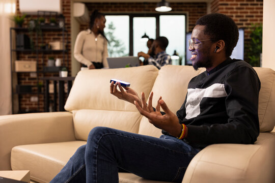 African american male entrepreneur wearing earphones using holographic interface while discussing business data. The cozy startup workspace buzzes with energy, innovation and professional teamwork.
