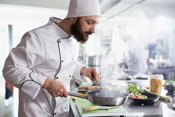 Steam rises from a sizzling pan as a male head chef prepares a tasty recipe in a modern restaurant...
