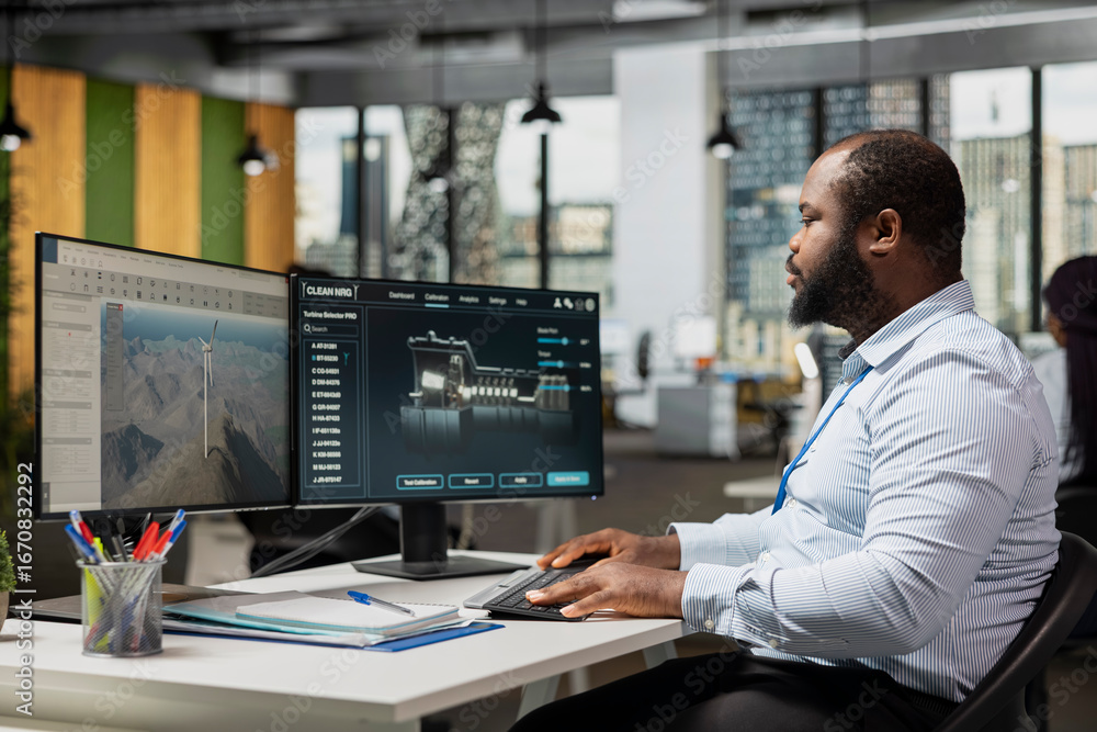 Poster engineer in office uses dual monitor setup to analyze turbine mechanics and windmill farm layouts. r