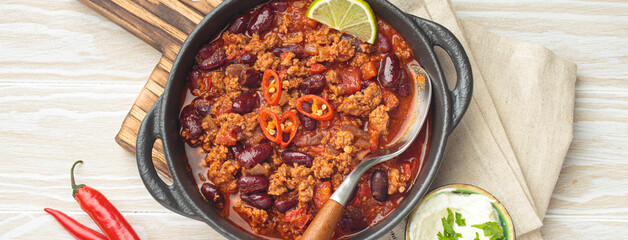 Traditional mexican chili con carne with lime, red chili peppers, and sour cream in a cast iron pan...