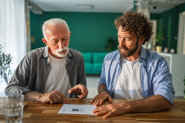Senior man scanning qr code with smart phone, son helping him at home