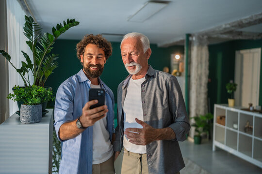 Senior father and adult son using smart phone at home - Powered by Adobe