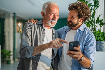 Adult son helping senior father using smart phone at home