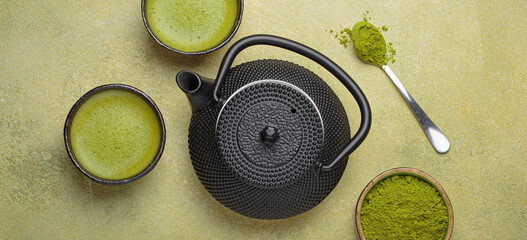 Matcha tea in cups, black iron teapot and matcha powder on a green background, a relaxing and...