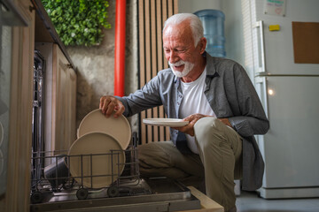 Elderly man loading dishwasher in modern kitchen
