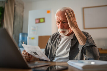 Worried senior man reading documents at home office desk