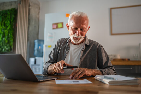 Senior man using magnifying glass reading documents at home office desk