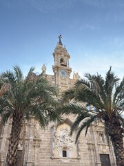 Church of San Juan through palm trees and blue sky on a sunny day in Plaza Mercat in Valencia, Spain. Valencia landmark.