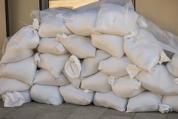 Stack of white sandbags placed in front of building entrance for flood protection and water barrier safety. Emergency preparedness, disaster prevention and property defense during heavy rain and storm