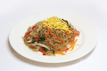 High resolution photo of colorful Korean japchae, stir-fried glass noodles with vegetables, served on a white plate over white background. Healthy and authentic Korean cuisine.