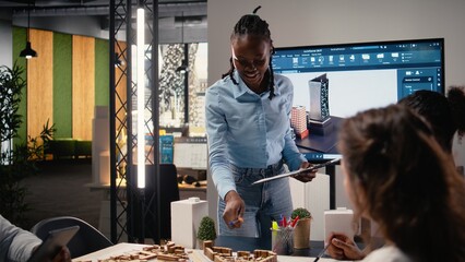 Black property developer discussing residential project investment and strategy for infrastructure growth and city planning in a bright office, analyzing blueprints and 3D models.
