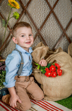 Smiling boy with red flowers kneeling next to a burlap sack in a rustic setting