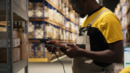 African American male employee scanning packages in a large warehouse, registering airway bills shipment details within industrial depot records. Using scanner for order fulfillment. Camera B.