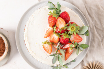 Bright overhead view of a delicious cake with white frosting, juicy strawberries, and eucalyptus, perfect for dessert and baking visuals