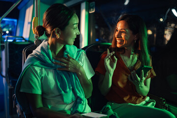 Two young women talking and using a smartphone on a night bus ride