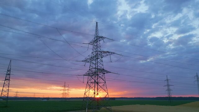 Power lines and pylons stretch across a sunset landscape, symbolizing sustainable energy and rural development. Aerial shot captures technology's harmony with nature.