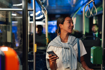 Young woman using smartphone on a public transport bus at night