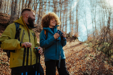 Hikers exploring autumn forest trail using binoculars and trekking poles