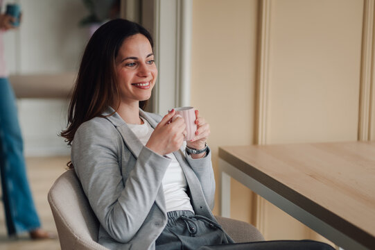 Businesswoman smiling and drinking coffee during break in office