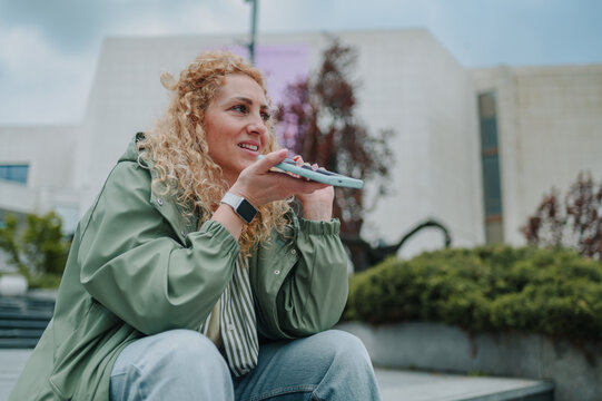 Smiling woman sending voice message outdoors using smartphone