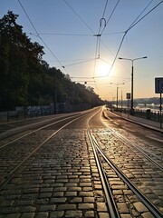 Fototapeta premium An empty road with tram tracks stretches out in Prague on a sunny morning, with the sun's reflection off the smooth cobblestones.