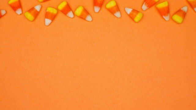 Halloween candy corn top border. Overhead view stop motion loop video over an orange background with copy space.